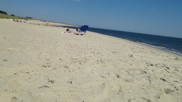 A sandy beach with a clear sky, a few people, and a blue beach chair.