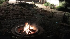 A backyard with a fire pit, outdoor furniture, and a house with multiple windows and a chimney.