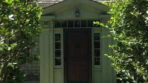 A small, single-story building with a green facade, a dark brown door, and a small porch area.