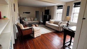 A spacious living room with hardwood flooring, a sofa, a chair, and a television.