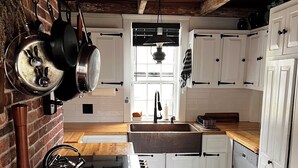 A rustic kitchen with wooden beams, white cabinets, and a brick wall.
