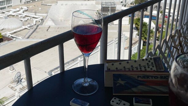 A balcony with a glass of red wine, dominoes, and a card game set.