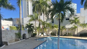 A swimming pool surrounded by palm trees and a white building.
