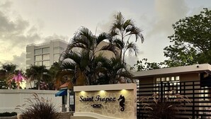 A sign for Saint Tropez with a beach view, palm trees, and a modern building in the background.
