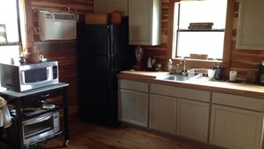 Una cocina con armarios de madera, un refrigerador negro, un microondas, un lavamanos y una ventana con vistas.