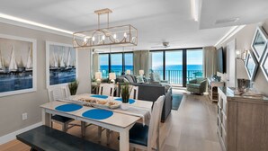 A modern living room with a dining area, large windows with a view of the sea, and a balcony with a view of the ocean.
