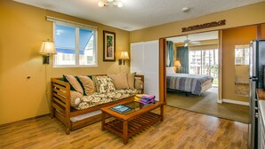 A cozy room with a sofa, a coffee table, and a bed. There are two lamps on the walls, and a ceiling fan is visible. - Surfer's Dream Condo w/ Full Kitchen - Free Wifi, Sleeps 4 (Honolulu)