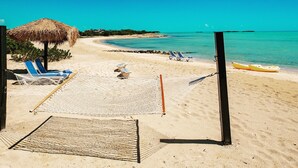 Een strand met een hangmat, ligstoelen en een rieten parasol.