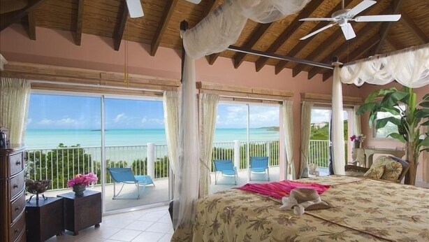Een slaapkamer met een groot bed, een plafondventilator en uitzicht op de oceaan door grote ramen.