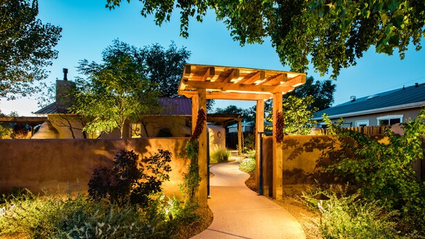 A wooden pergola with a curved pathway leading to a house.
