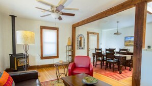 A living room with a fireplace, a red chair, wooden dining table, and a ceiling fan.
