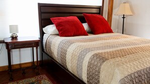 A neatly made bed with a patterned quilt, two red pillows, and a wooden headboard.