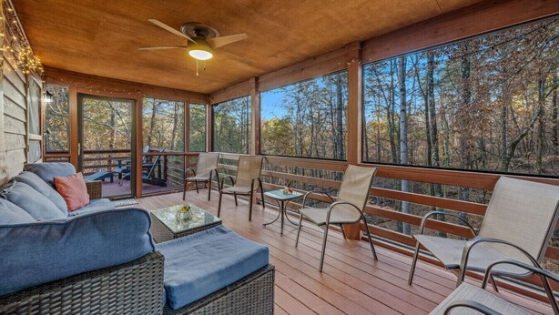 Un espace extérieur abrité, aménagé avec des meubles en osier, un ventilateur de plafond et offrant une vue sur une forêt.