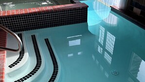 Une piscine avec un bord carrelé, un plongeoir et une fenêtre.