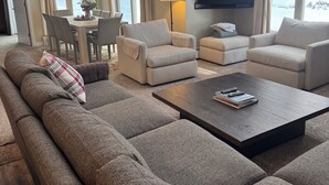 Un salon spacieux comprenant un grand canapé d’angle, deux fauteuils, une table basse et un coin repas agrémenté d’un lustre.