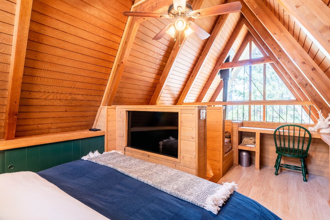 Um quarto de sótão acolhedor com paredes de madeira, teto inclinado, uma cama, um pequeno espaço de estar e uma janela.