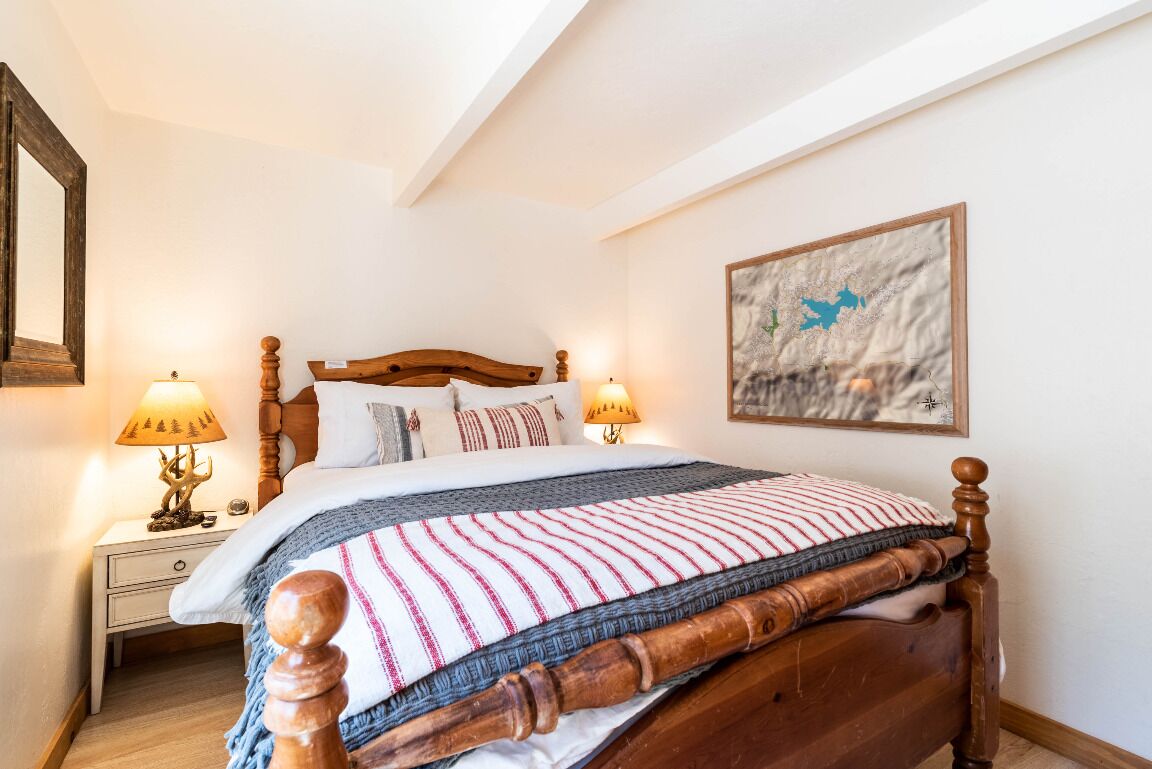 A neatly made bed with a wooden headboard, two bedside lamps, and a framed map on the wall.