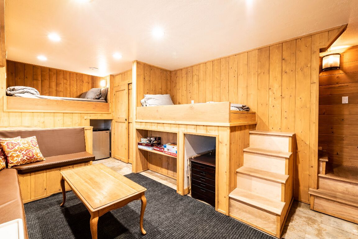 L’intérieur d’un chalet en bois chaleureux et accueillant, avec un lit superposé, un canapé, une petite table et un escalier.