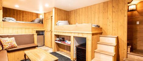 L’intérieur d’un chalet en bois chaleureux et accueillant, avec un lit superposé, un canapé, une petite table et un escalier.
