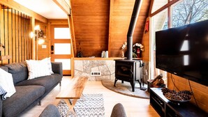 A cozy living room with a sofa, a coffee table, a fireplace, and a TV. - Mountain A-Frame, Wall of Glass w/Stunning Tree Views, Hot Tub, Firepit, Dogs ok (Lake Arrowhead)