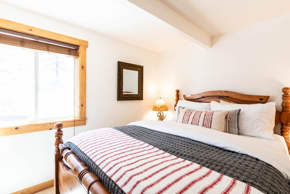Un dormitorio con una cama de madera, una ventana con persianas, una lámpara de noche y un espejo en la pared.