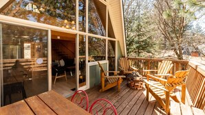 A wooden deck with outdoor seating and a glass door leading to an interior space. - Mountain A-Frame, Wall of Glass w/Stunning Tree Views, Hot Tub, Firepit, Dogs ok (Lake Arrowhead)