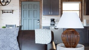 A modern living room with a dark leather sofa, a round side table with a lamp, and a kitchen in the background. - Unreal Views GSMNP/Near DwTn Gatlinburg/Hot Tub (Gatlinburg)