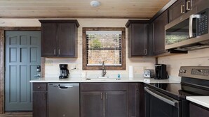 A compact kitchen with dark wooden cabinets, a built-in microwave, a dishwasher, and a window with blinds. - Unreal Views GSMNP/Near DwTn Gatlinburg/Hot Tub (Gatlinburg)