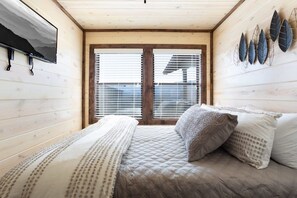 A bedroom with a bed, a window with blinds, and a wall-mounted TV.
