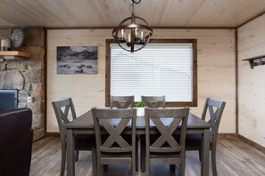 A dining area with a wooden table and chairs, a chandelier, a stone wall, and a window with blinds. - Unreal Views GSMNP/Near DwTn Gatlinburg/Hot Tub (Gatlinburg)