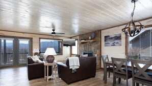 A spacious living room with a brown sofa, a small table with a lamp, and a dining area with a wooden table and chairs. - Unreal Views GSMNP/Near DwTn Gatlinburg/Hot Tub (Gatlinburg)