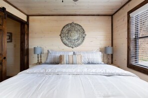 Un dormitorio con una cama grande, dos lámparas de noche, un adorno de pared y una ventana con persianas.
