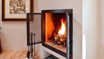 Una chimenea con un reloj encima, un cuadro en la pared y una alfombra estampada en el suelo.