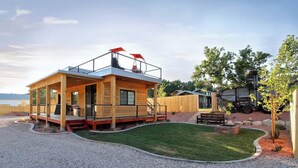 A wooden cabin with a balcony, a gravel driveway, and a lawn. - Tiny Home near Zion with Rooftop Stargazing Deck (Orderville)