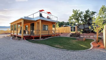 A wooden cabin with a balcony, a gravel driveway, and a lawn.