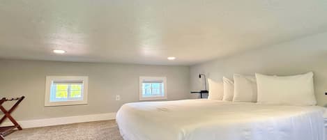 A bedroom with a large bed, two windows, a ceiling fan, and a wooden chair.