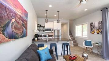 A modern living room with a sofa, a coffee table, and a dining area with bar stools.