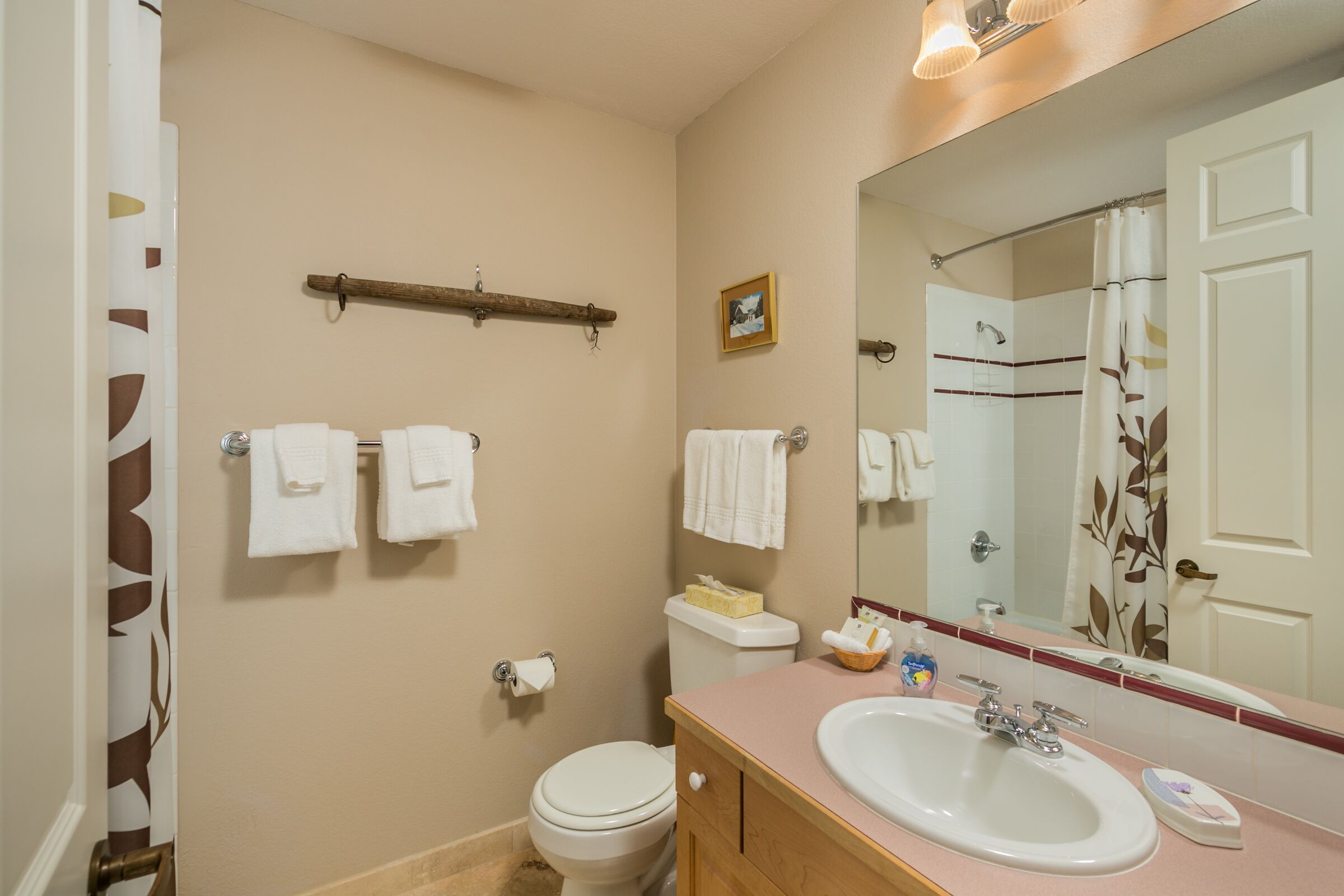 A bathroom with a toilet, sink, and mirror. There are towels hanging on the wall and a shelf above the toilet.
