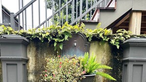 A concrete planter with various plants, a metal water spout, and a staircase railing.