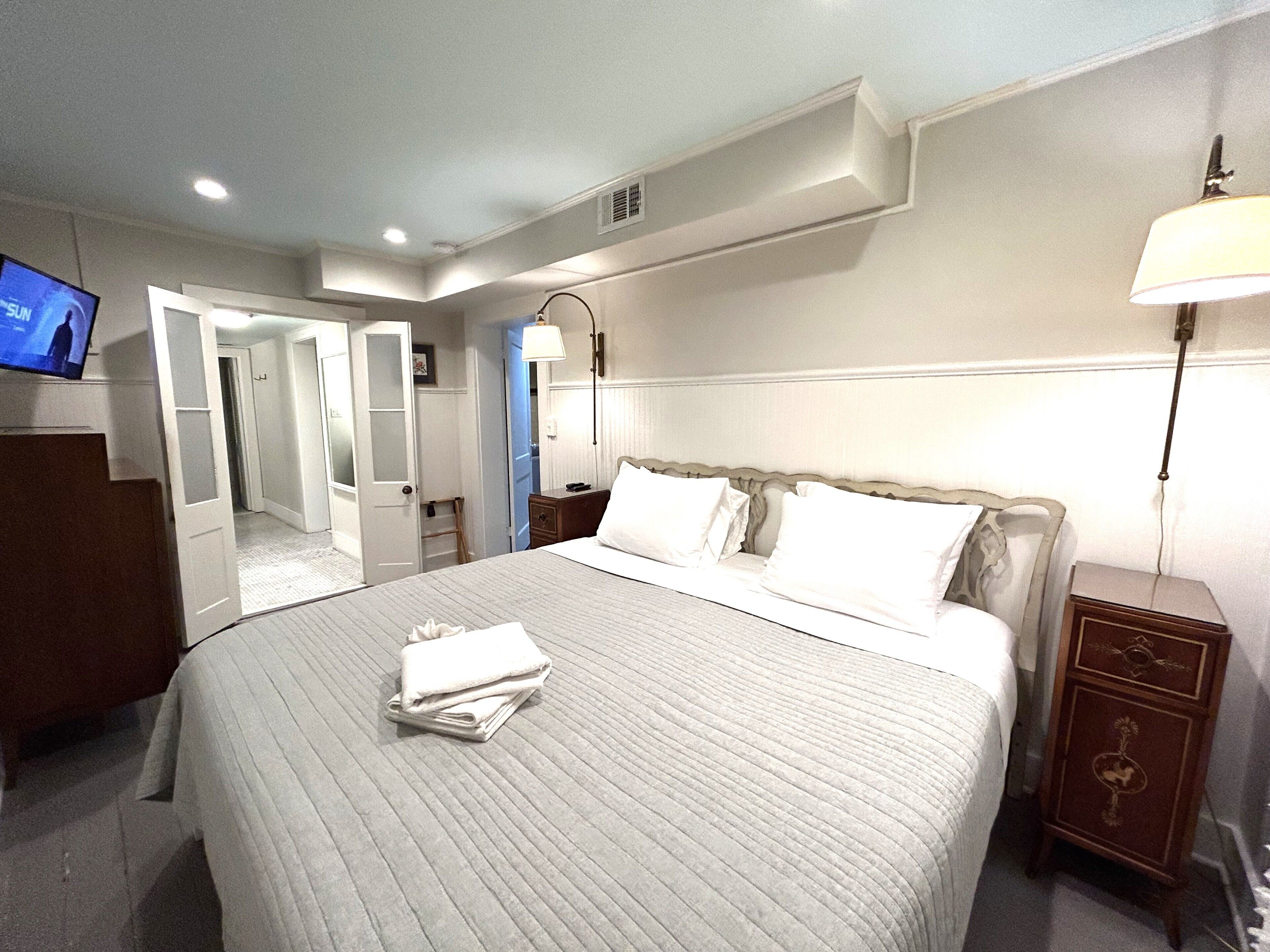 Een hotelkamer met een groot bed, een televisie links, een nachtkastje met een lamp en een garderobe.