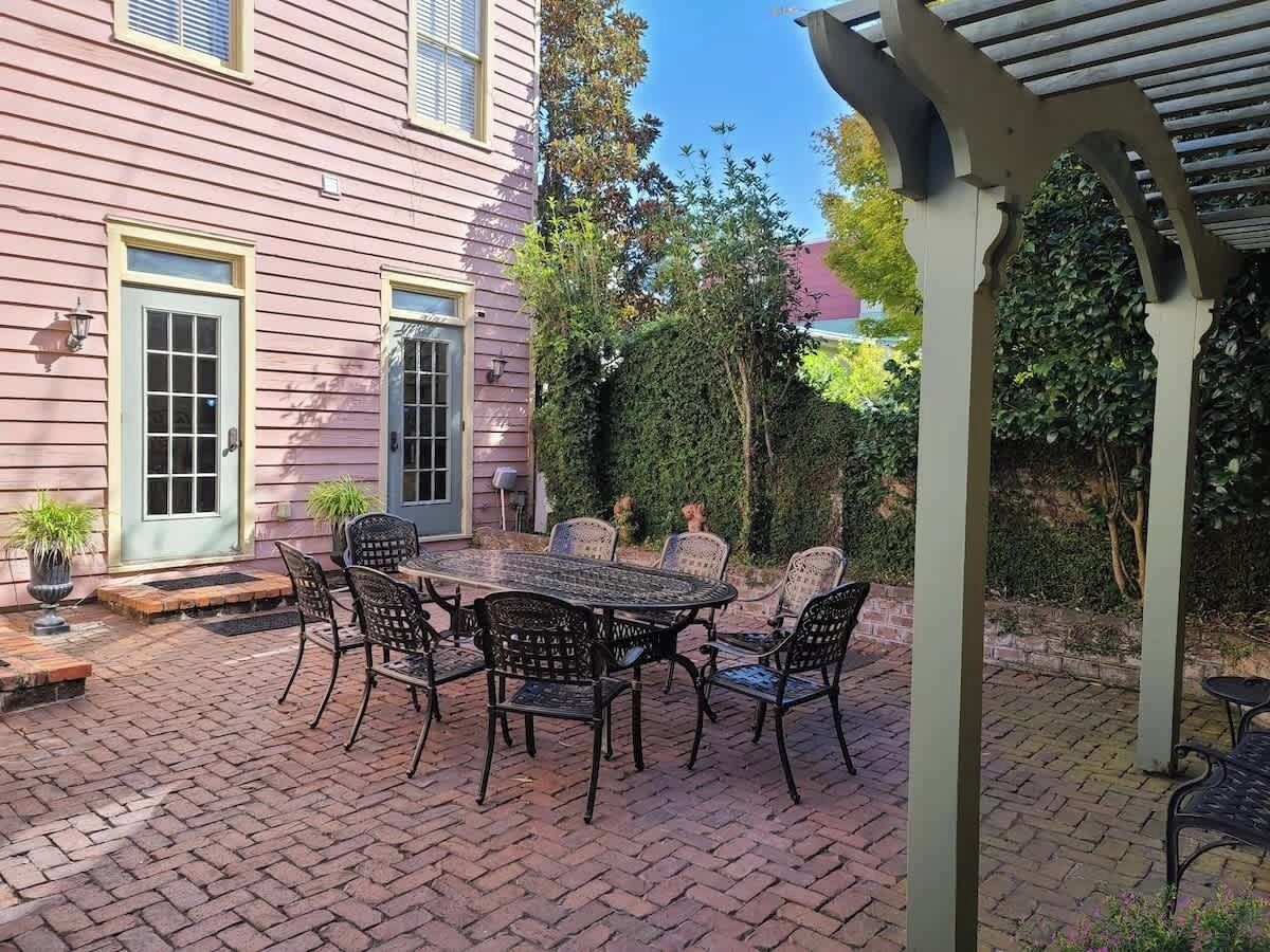 Un patio con mesa y sillas, una zona cubierta y una casa con puerta y ventanas.