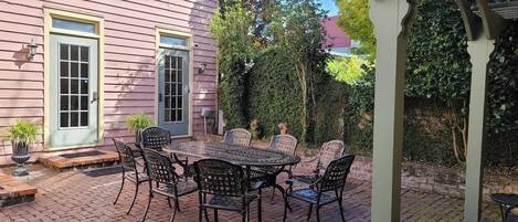 Un patio con mesa y sillas, una zona cubierta y una casa con puerta y ventanas.