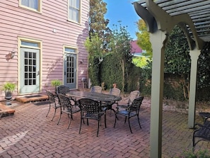 Un patio con mesa y sillas, una zona cubierta y una casa con puerta y ventanas.