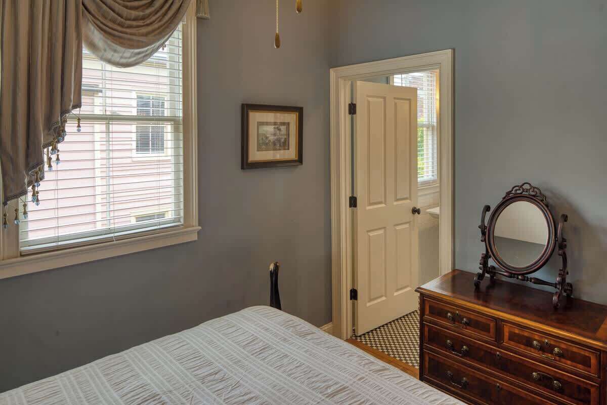 A bedroom with a bed, dresser, mirror, and a door leading to another room.