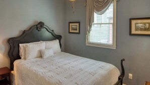 A bedroom with a dark wooden bed frame, a white bedspread, and a window with curtains.