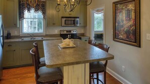 A kitchen with a central island, a microwave, a stove, and a chandelier.