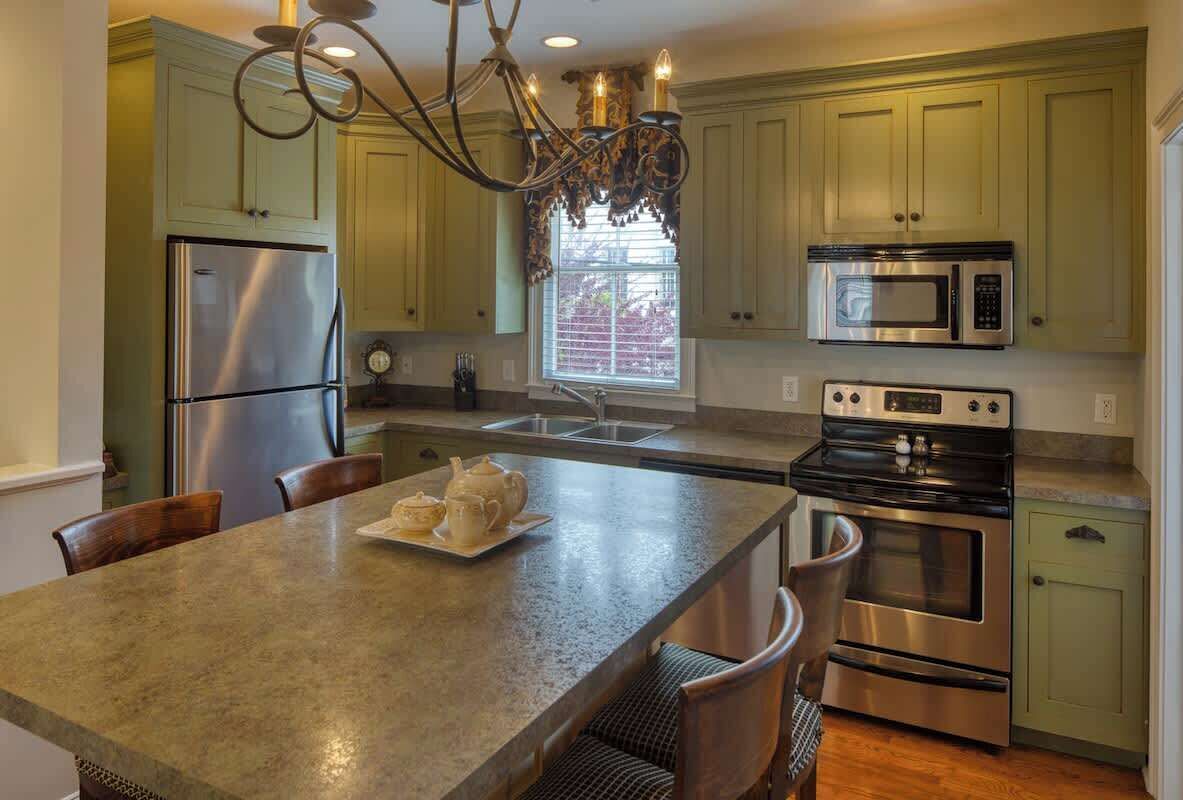 A kitchen with a central island, stainless steel appliances, and light green cabinetry.