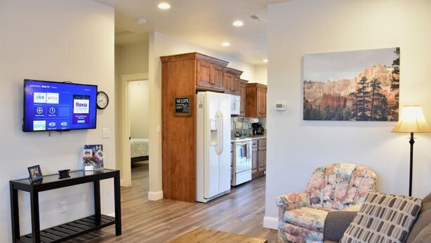 A living room with a flat-screen TV, a wooden coffee table, a floral armchair, and a painting of a mountainous landscape.