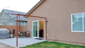 A residential backyard with a covered patio, a barbecue grill, and a sliding glass door leading to a covered patio area.