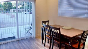A room with a wooden table and chairs, a window with blinds, and an exit sign.
